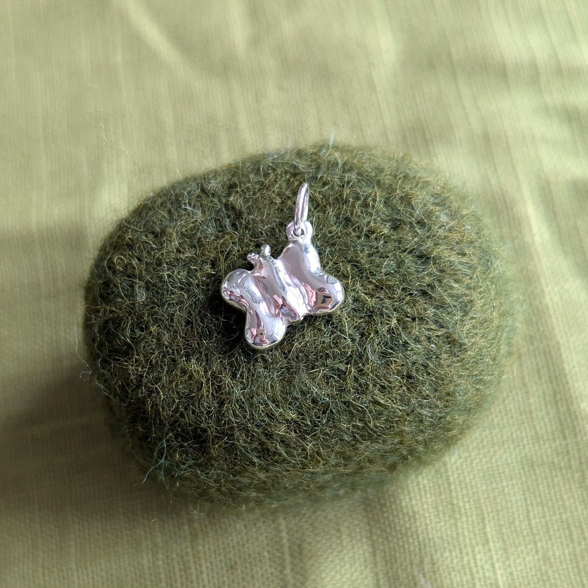 Small  silver butterfly pendant on a textured green surface